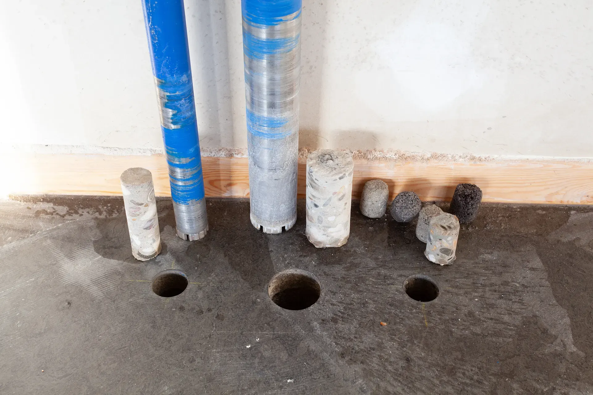 Kärnborrade betongcylindrar och borrkronor bredvid borrade hål i golv.